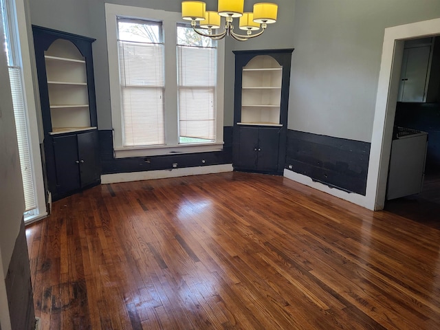 unfurnished dining area featuring built in shelves, a wealth of natural light, dark hardwood / wood-style flooring, and a chandelier