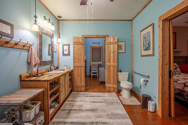 bathroom featuring ornamental molding, vanity, ceiling fan, wood-type flooring, and toilet