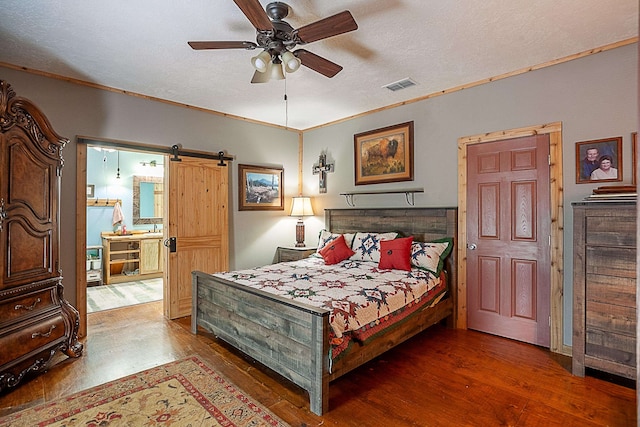 bedroom featuring a textured ceiling, a barn door, dark hardwood / wood-style floors, and ceiling fan