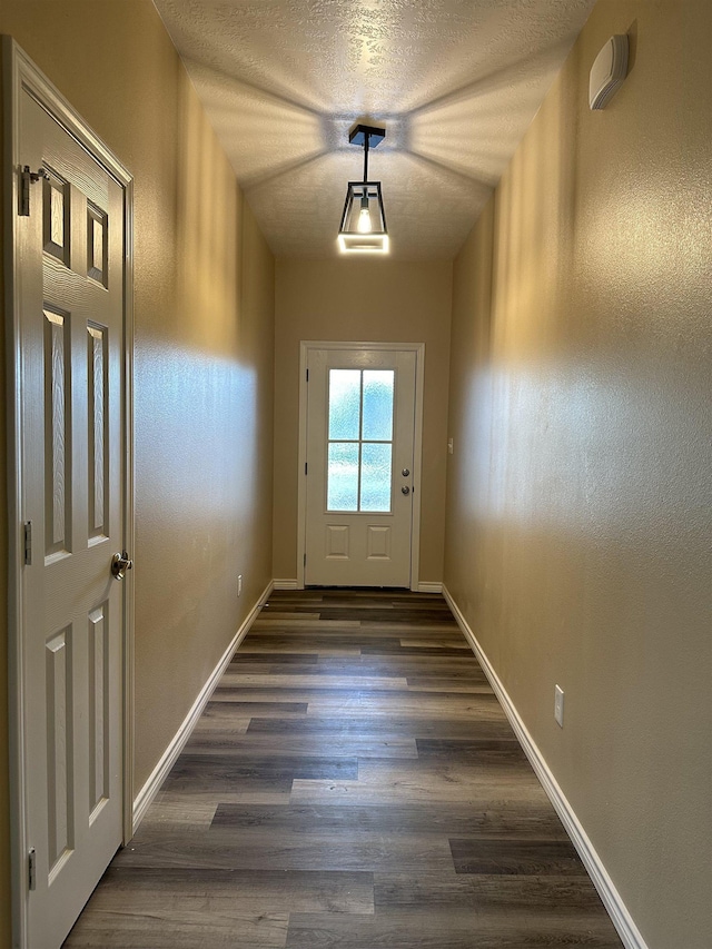 doorway to outside with dark wood-type flooring, baseboards, and a textured ceiling