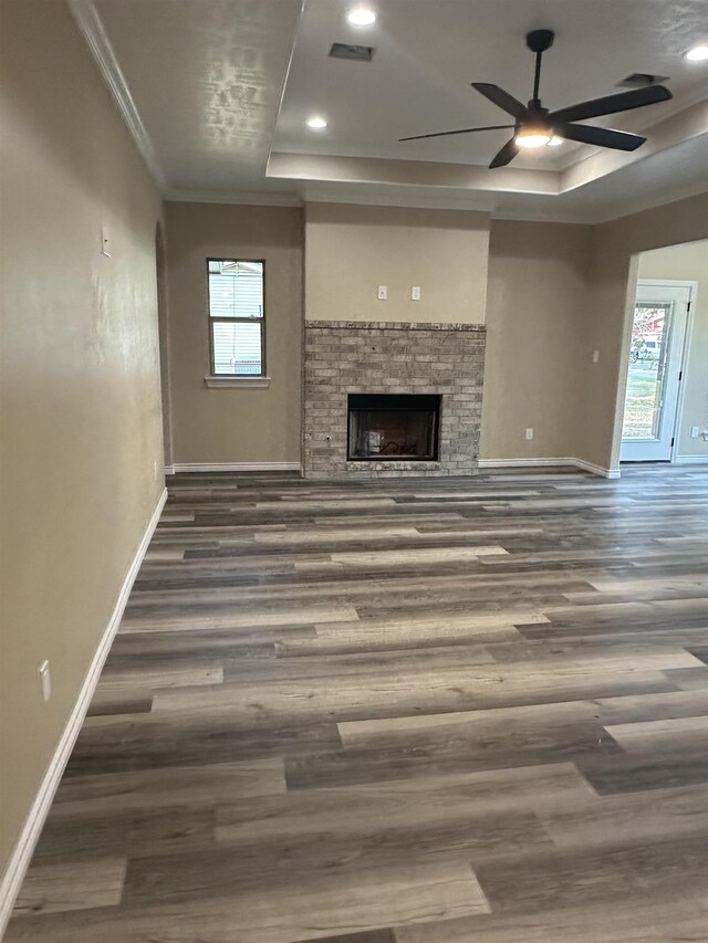 unfurnished living room with ceiling fan, dark wood-type flooring, a raised ceiling, crown molding, and a fireplace