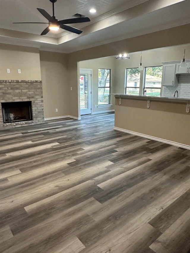 unfurnished living room featuring dark hardwood / wood-style floors, ceiling fan, a raised ceiling, and a fireplace