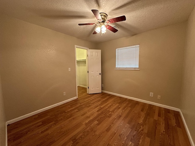 unfurnished bedroom with a textured ceiling, ceiling fan, wood-type flooring, a spacious closet, and a closet