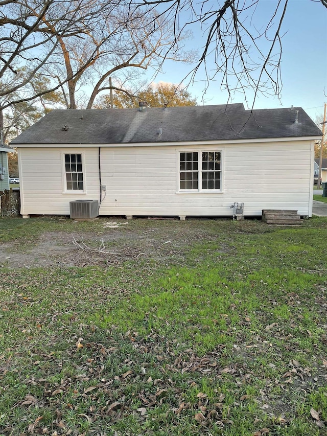 rear view of house with central air condition unit and a lawn