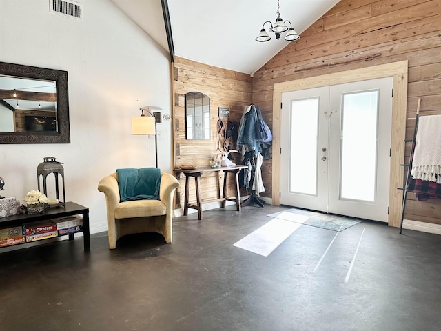 entryway featuring an inviting chandelier, french doors, wooden walls, vaulted ceiling, and concrete floors