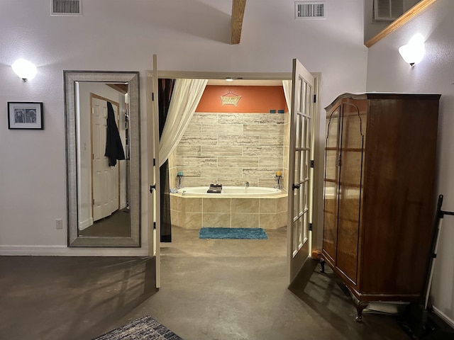 bathroom with beamed ceiling, a relaxing tiled tub, and concrete flooring