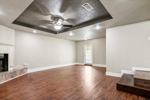 unfurnished living room with a tray ceiling, ceiling fan, dark wood-type flooring, and a textured ceiling