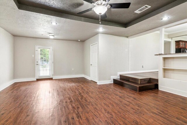 empty room featuring a tray ceiling, ceiling fan, dark wood-type flooring, and a textured ceiling