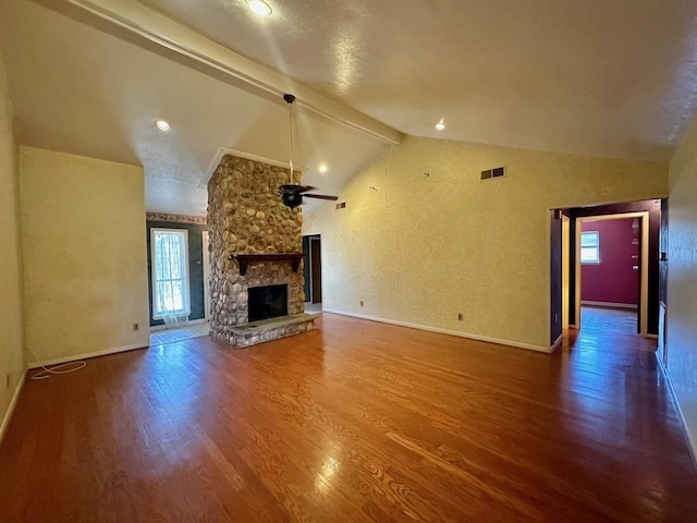 unfurnished living room featuring ceiling fan, a healthy amount of sunlight, wood-type flooring, lofted ceiling with beams, and a fireplace