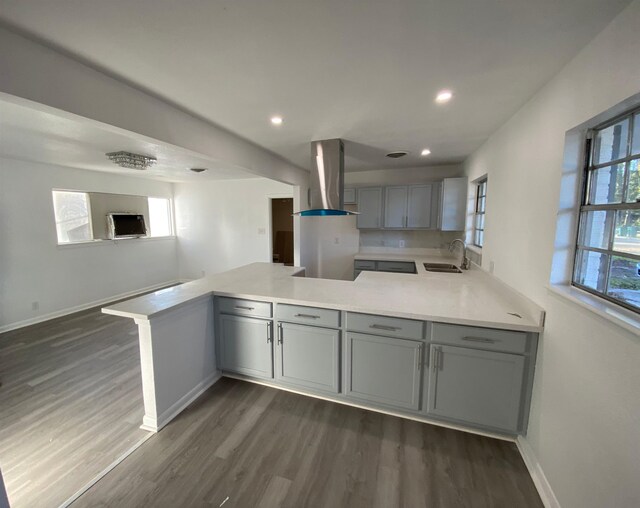 kitchen featuring sink, a healthy amount of sunlight, wall chimney range hood, kitchen peninsula, and gray cabinets