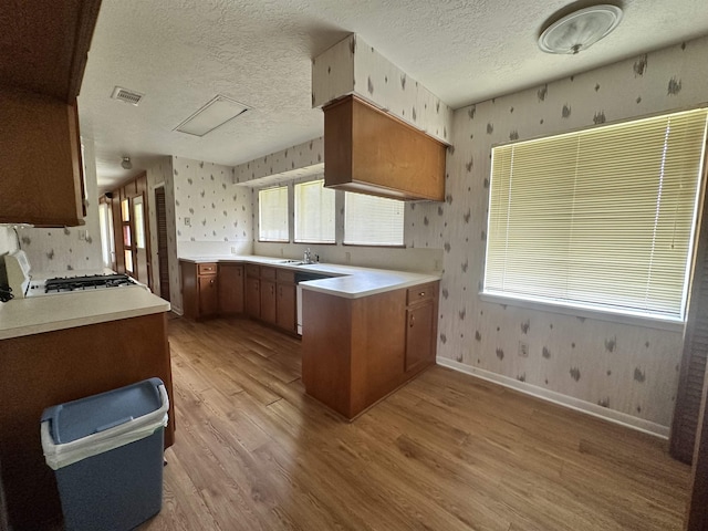 kitchen with wallpapered walls, a peninsula, visible vents, and light wood-type flooring