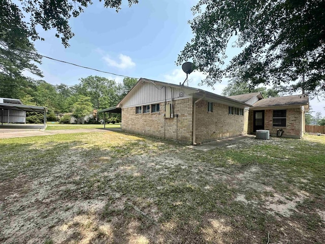 view of home's exterior with an attached carport, brick siding, central AC, and a yard