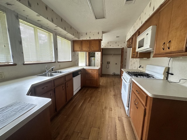 kitchen featuring brown cabinets, white appliances, wallpapered walls, and a sink