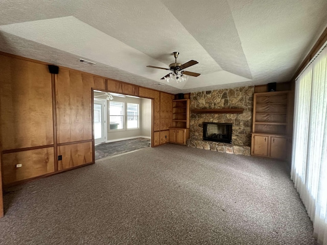 unfurnished living room featuring visible vents, a textured ceiling, carpet, a stone fireplace, and ceiling fan