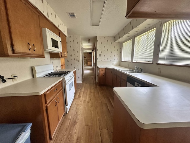 kitchen featuring brown cabinets, a sink, a textured ceiling, white appliances, and wallpapered walls