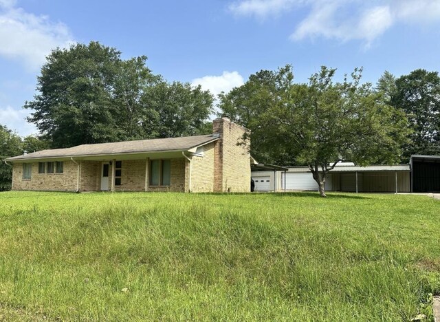 view of front of home with a chimney, a carport, a front lawn, a garage, and brick siding