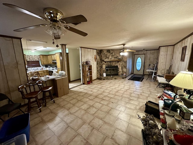 living room featuring a fireplace, a textured ceiling, ceiling fan, and wood walls