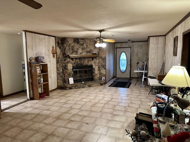 living room with a textured ceiling, ceiling fan, crown molding, a stone fireplace, and wood walls