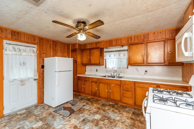 kitchen with ceiling fan, sink, a textured ceiling, white appliances, and wooden walls