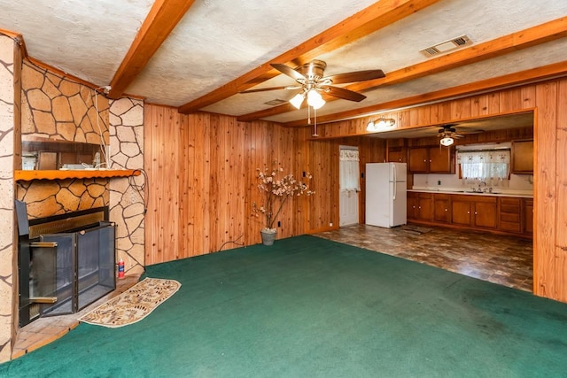 unfurnished living room with ceiling fan, wood walls, a stone fireplace, and sink