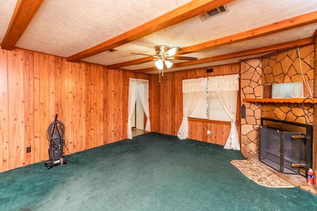 unfurnished living room featuring carpet flooring, beam ceiling, a textured ceiling, and a stone fireplace