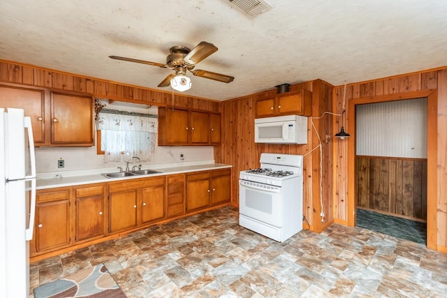 kitchen with a textured ceiling, white appliances, ceiling fan, sink, and wood walls