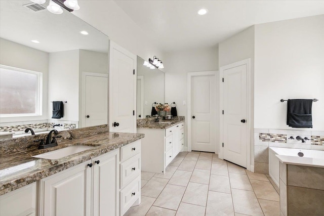 bathroom with tile patterned flooring, visible vents, a washtub, two vanities, and a sink