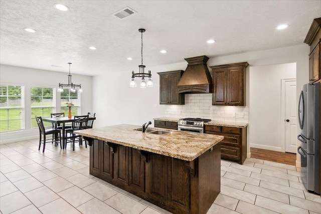 kitchen featuring visible vents, custom exhaust hood, a notable chandelier, stainless steel appliances, and a sink