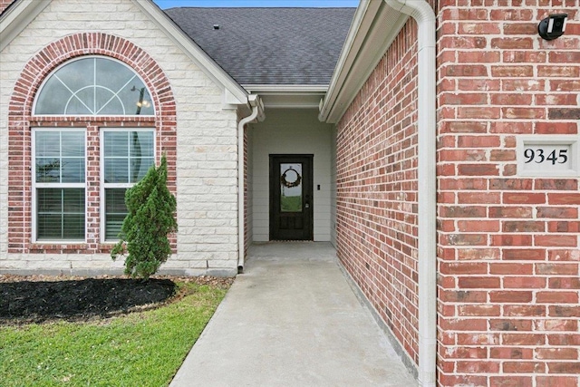 entrance to property with brick siding and a shingled roof