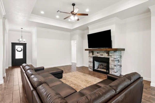 living room featuring a stone fireplace, a raised ceiling, ceiling fan with notable chandelier, and ornamental molding