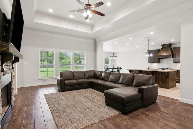 living room featuring dark wood-style floors, ceiling fan with notable chandelier, crown molding, and a tray ceiling