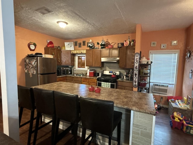 kitchen featuring a kitchen bar, dark hardwood / wood-style flooring, a textured ceiling, stainless steel appliances, and cooling unit