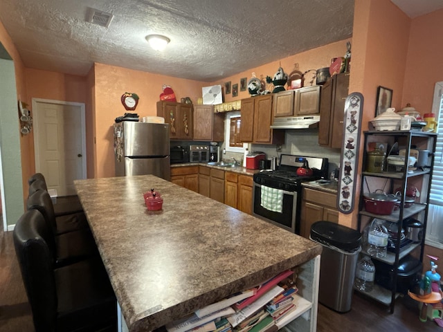 kitchen with dark wood-type flooring, sink, a textured ceiling, a kitchen island, and stainless steel appliances