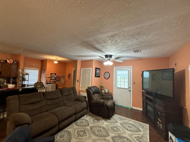 living room with a textured ceiling, ceiling fan, and dark wood-type flooring