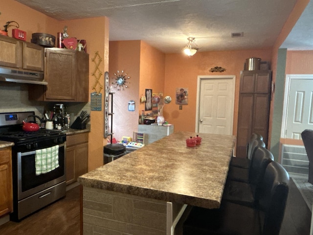 kitchen with a kitchen bar, dark hardwood / wood-style flooring, a center island, and stainless steel stove