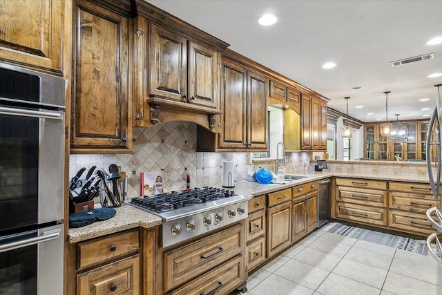 kitchen with light tile patterned flooring, appliances with stainless steel finishes, sink, hanging light fixtures, and light stone counters