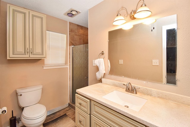 bathroom featuring wood-type flooring, a textured ceiling, toilet, a shower with door, and vanity