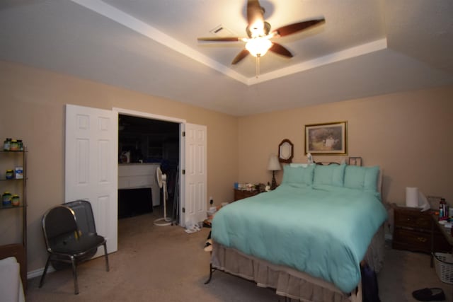 carpeted bedroom featuring a tray ceiling, a walk in closet, and ceiling fan