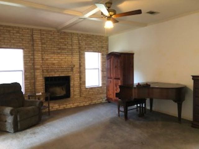 interior space featuring dark carpet, a fireplace, ceiling fan, crown molding, and beamed ceiling