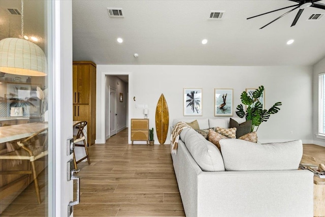 living room with ceiling fan, light wood finished floors, and visible vents