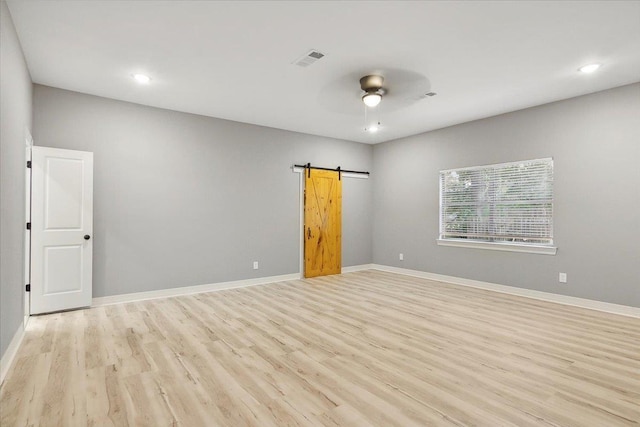 spare room with a barn door, ceiling fan, and light hardwood / wood-style floors