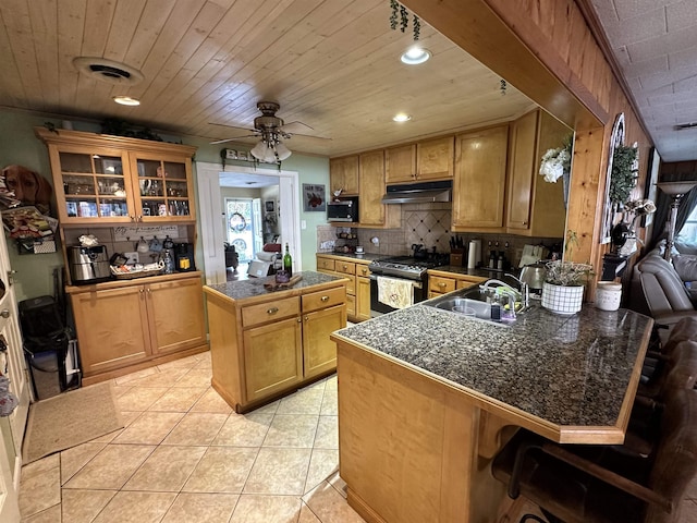 kitchen featuring sink, stainless steel gas range oven, kitchen peninsula, a breakfast bar area, and a kitchen island