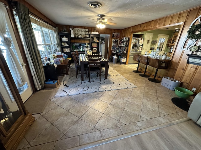 dining room with ceiling fan, light tile patterned floors, and wooden walls