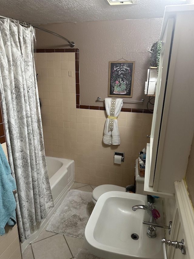 full bathroom featuring sink, tile patterned floors, shower / bath combination with curtain, a textured ceiling, and tile walls