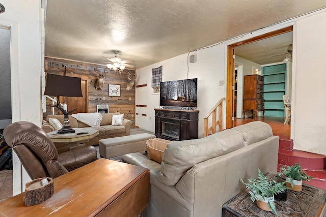 living room featuring ceiling fan, a textured ceiling, and wooden walls