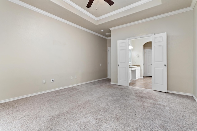 unfurnished bedroom featuring connected bathroom, ceiling fan, a raised ceiling, light colored carpet, and ornamental molding