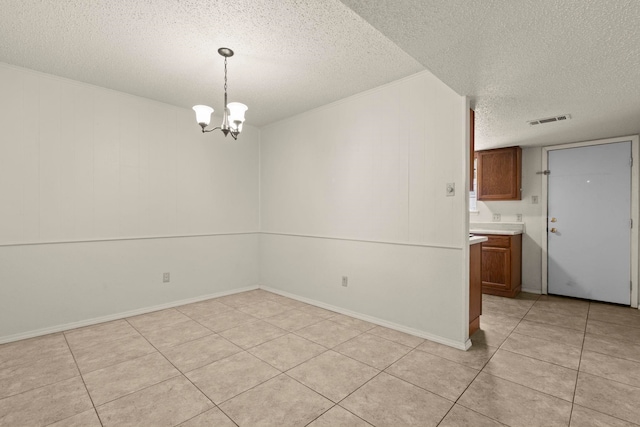 empty room with a chandelier, a textured ceiling, visible vents, and light tile patterned floors