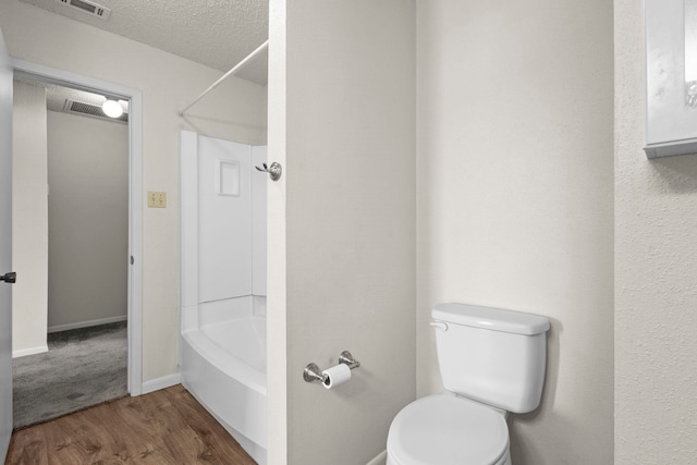 bathroom with wood finished floors, a textured ceiling, toilet, visible vents, and bathing tub / shower combination
