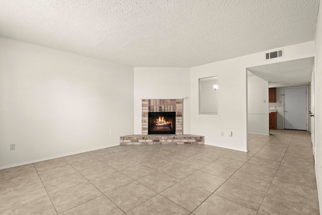 unfurnished living room featuring visible vents, light tile patterned flooring, baseboards, a fireplace, and a textured ceiling