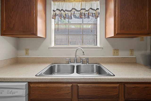 kitchen with light countertops, white dishwasher, a sink, and brown cabinets